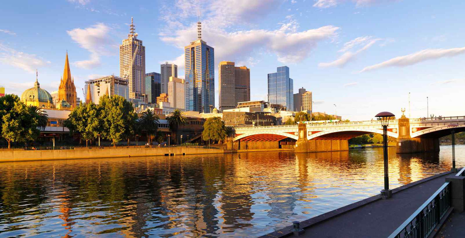 Sunny day over the Yarra River in Melbourne, with a view towards Princes Bridge, the city skyline, and scattered clouds in the blue sky.