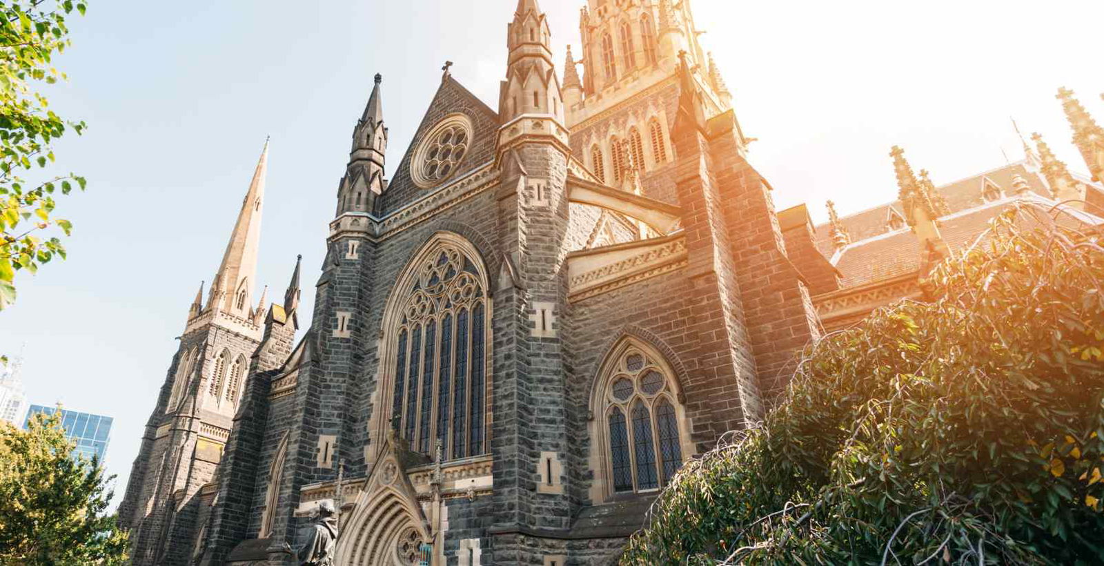 Sunlight streaming down on the front exterior of St. Patrick's Cathedral in Melbourne, highlighting its majestic Gothic architecture against a clear blue sky.