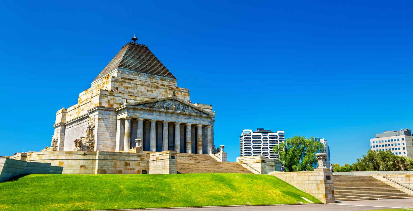 Front view of the Shrine of Remembrance in Melbourne, featuring its grand architecture surrounded by a vibrant green grassy lawn under a clear sky.