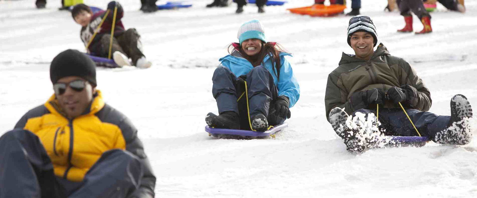 A group of people joyfully sledding down a snowy hill, surrounded by a winter landscape.