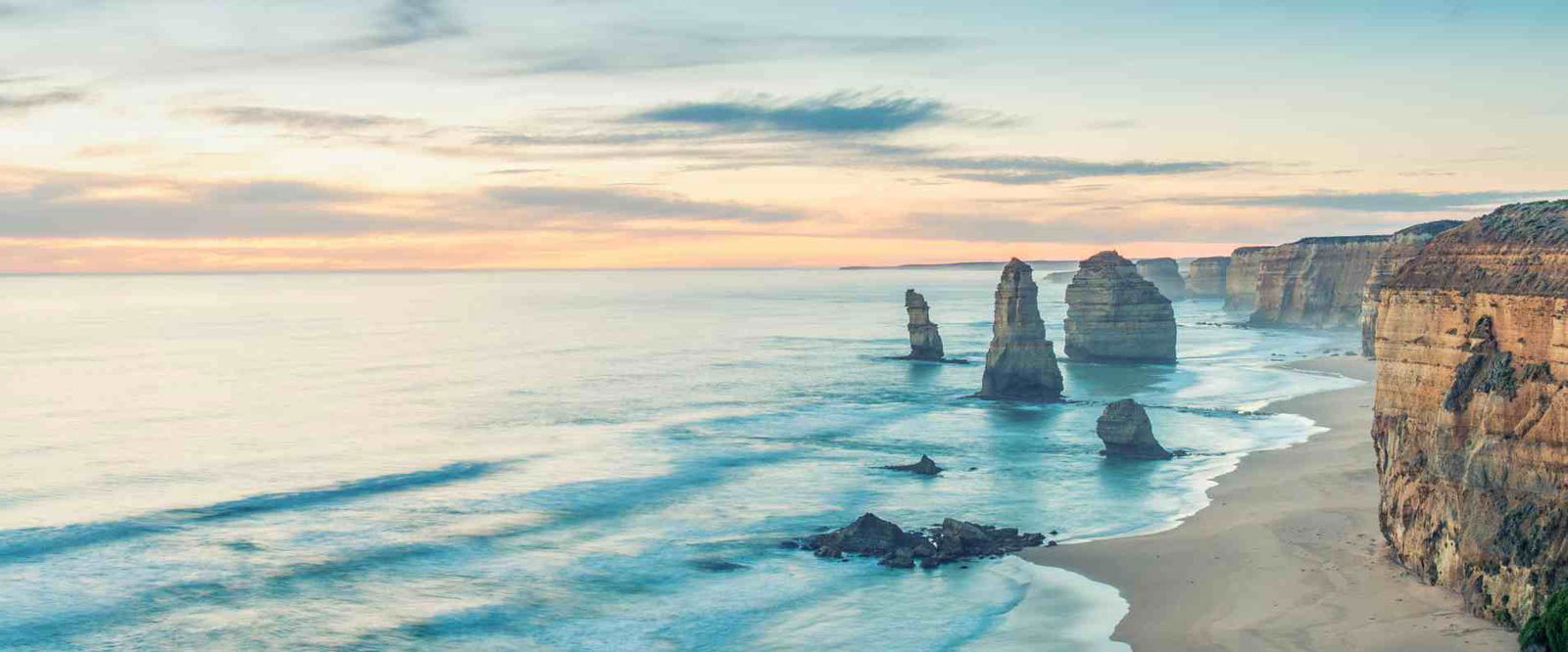 The Twelve Apostles at sunset, featuring stunning rock formations along the Great Ocean Road illuminated by warm hues.