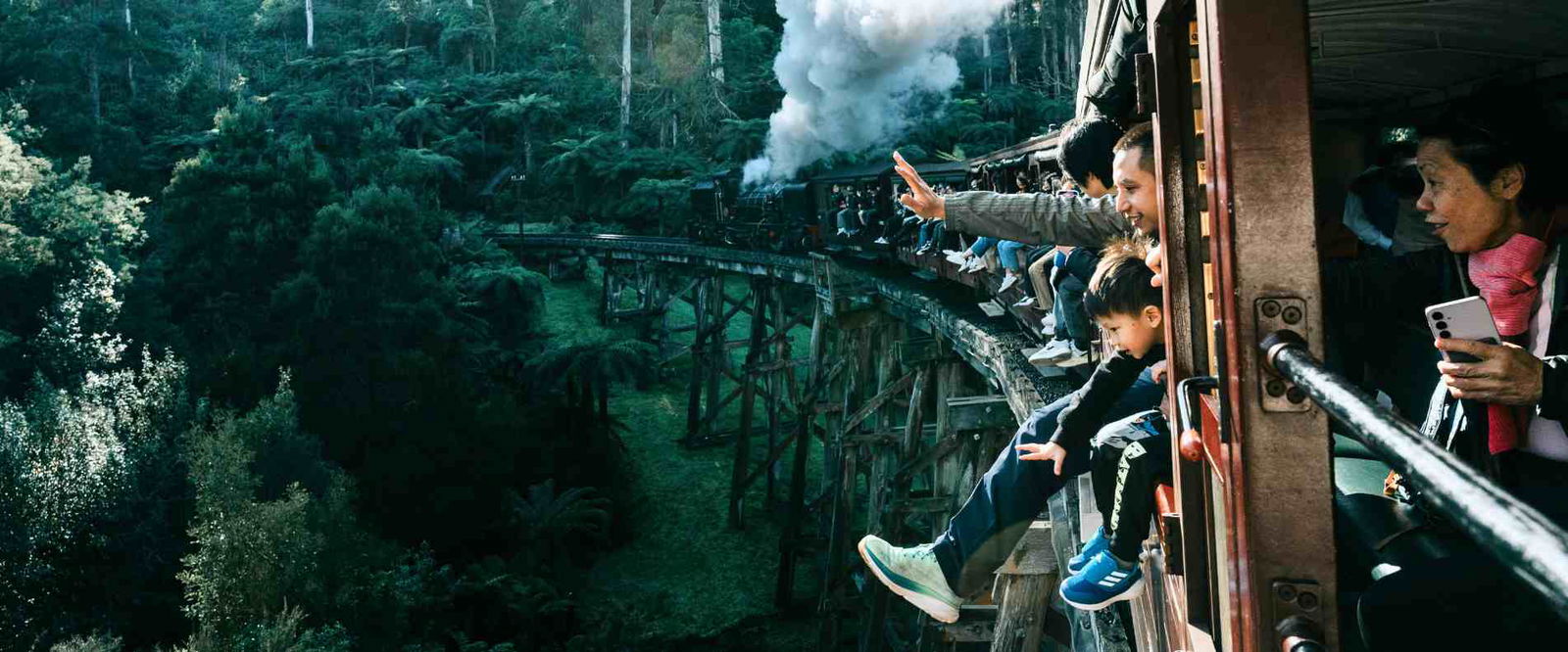 people hanging legs over puffing billy steam train 